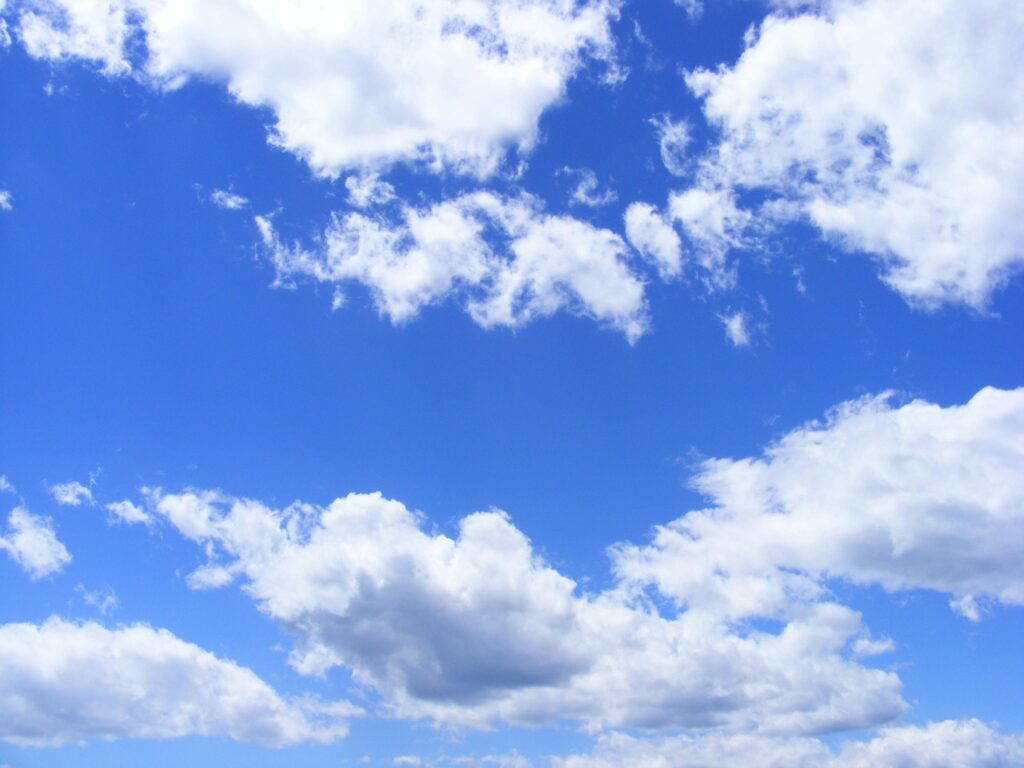 Vibrant cumulus clouds adorn a clear blue sky, creating a serene and dreamy cloudscape.