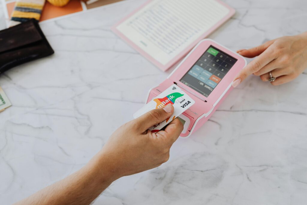 Hands making a contactless payment using a credit card and a pink terminal on a marble table.